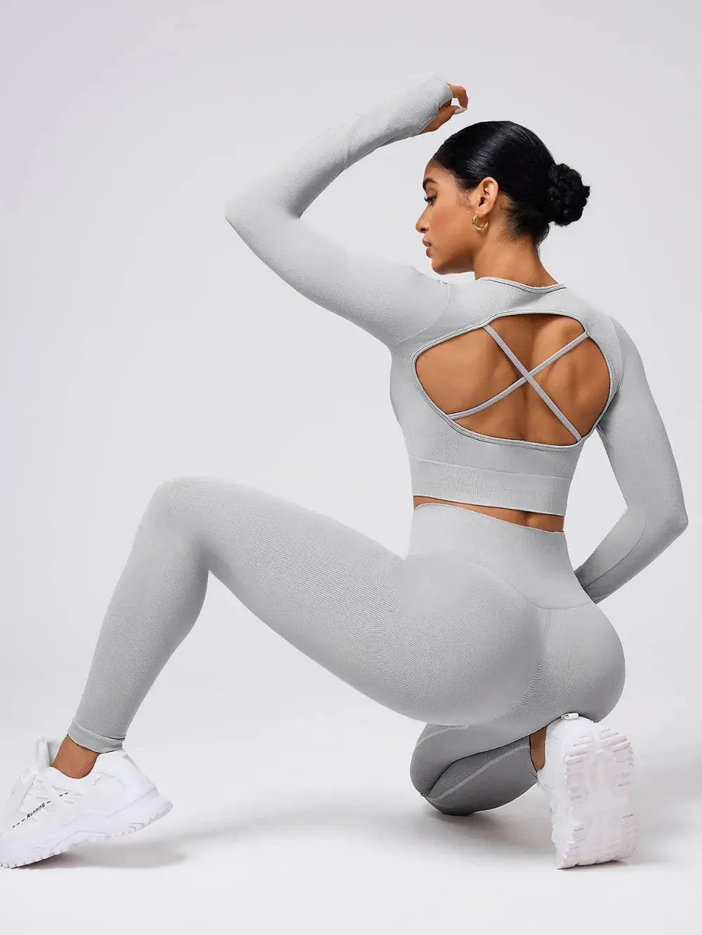Woman wearing light gray back crisscross long sleeve crop top and matching leggings active set