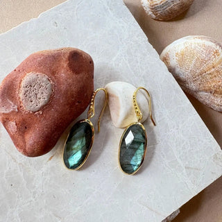 Charis Oval Gemstone Earrings with labradorite stones set in 22K gold on recycled brass, displayed with natural stones