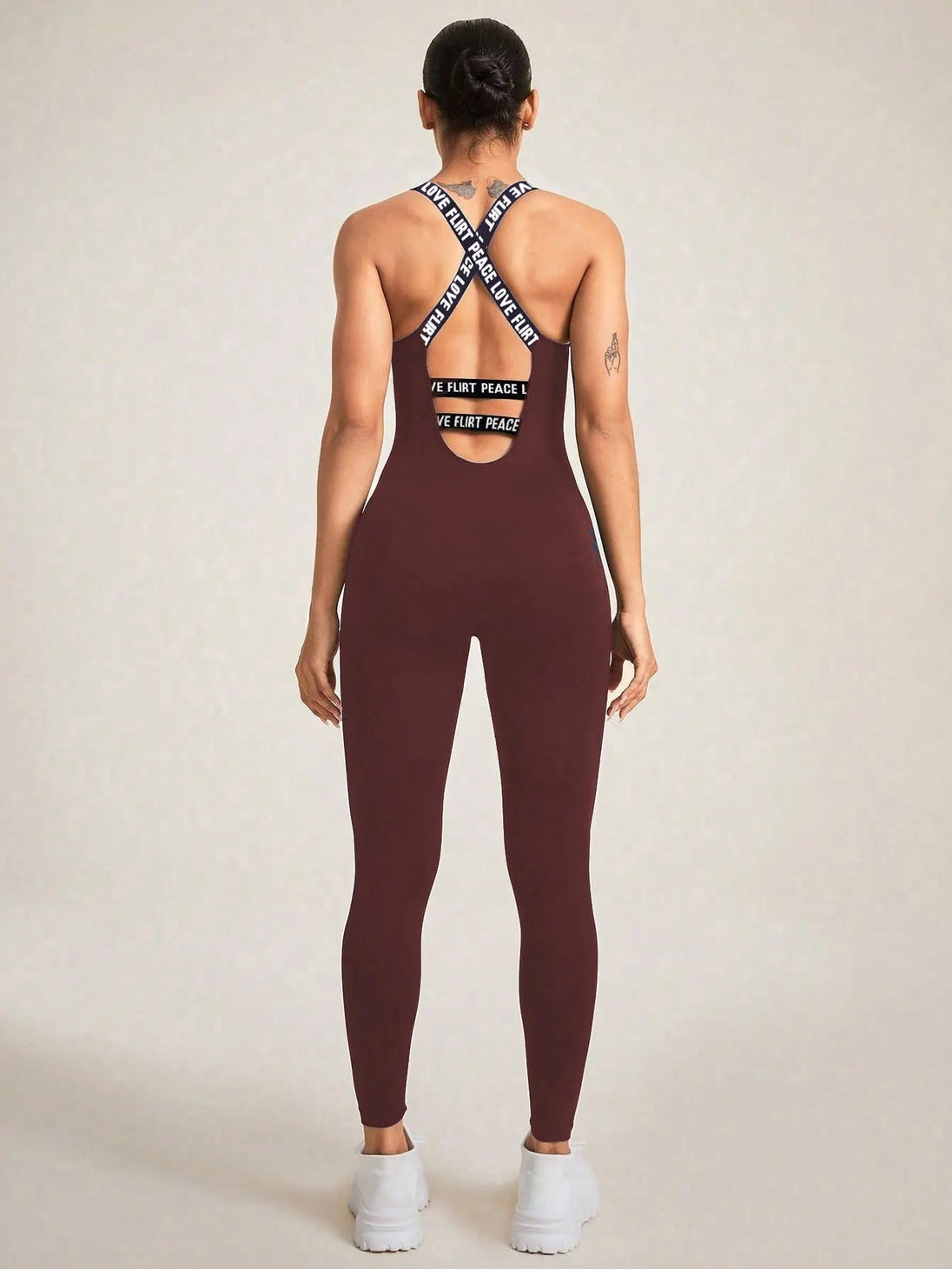Back view of woman wearing seamless camisole jumpsuit in dark brown with crossed straps and athletic fit