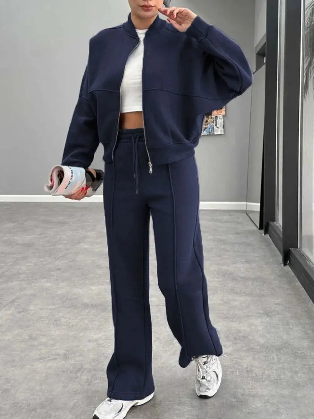 Woman wearing navy baseball collar zip up outerwear and drawstring pants set with white sneakers in modern room