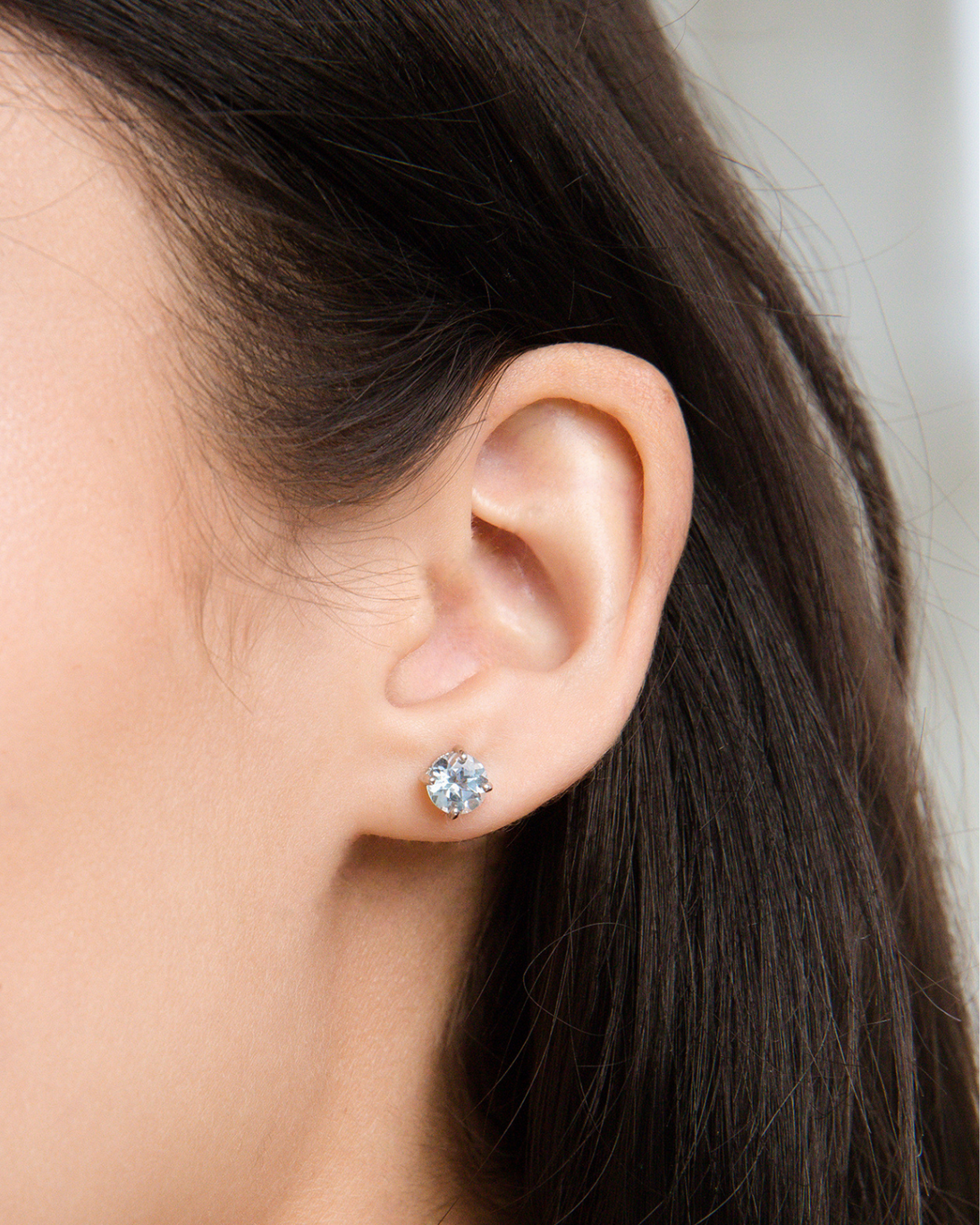 Close-up of a woman's ear wearing a sky blue topaz stud earring from a handcrafted sterling silver blue topaz everyday jewellery set
