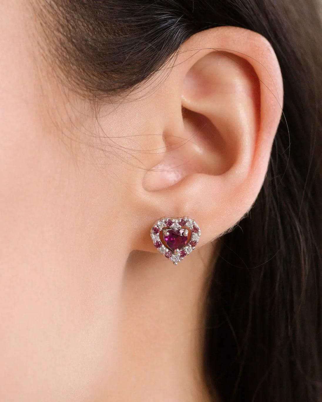 Close-up of a red heart rhodolite garnet stud earring in sterling silver worn on an ear