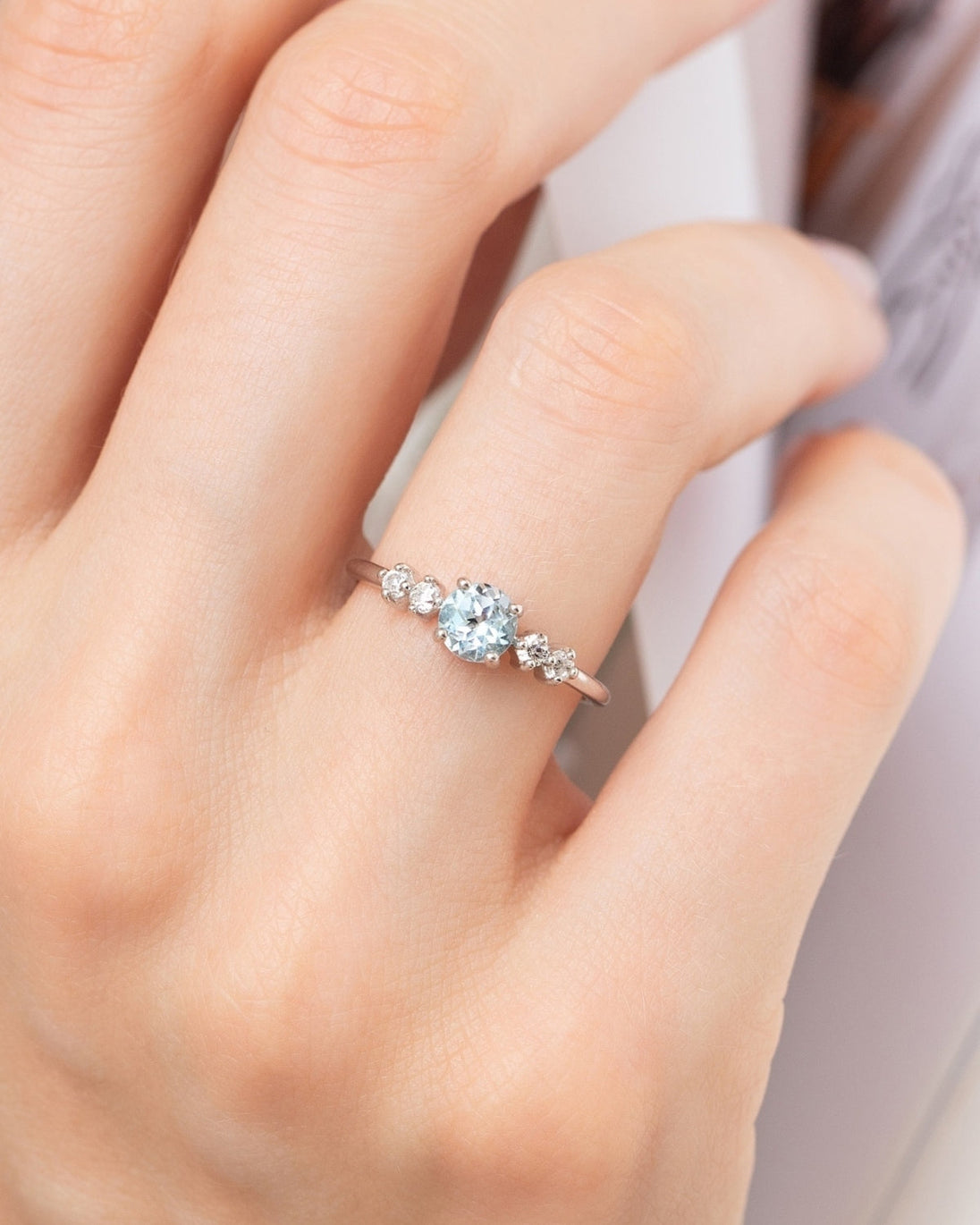 Hand wearing blue topaz ring with round cut sky blue gemstone and simulated diamonds in sterling silver