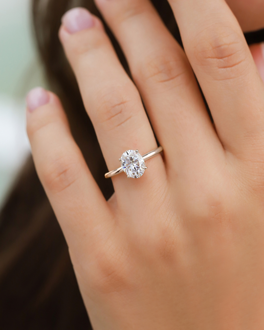 Close-up of 2 ct oval solitaire moissanite ring on finger with sterling silver band