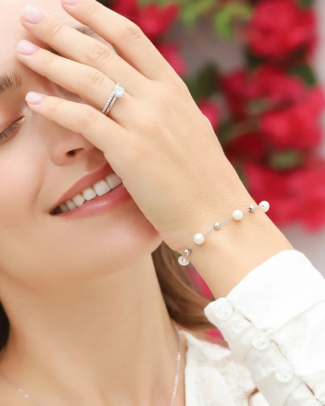 Woman wearing a sterling silver pearl bracelet with natural freshwater pearls and silver balls, smiling with eyes closed.