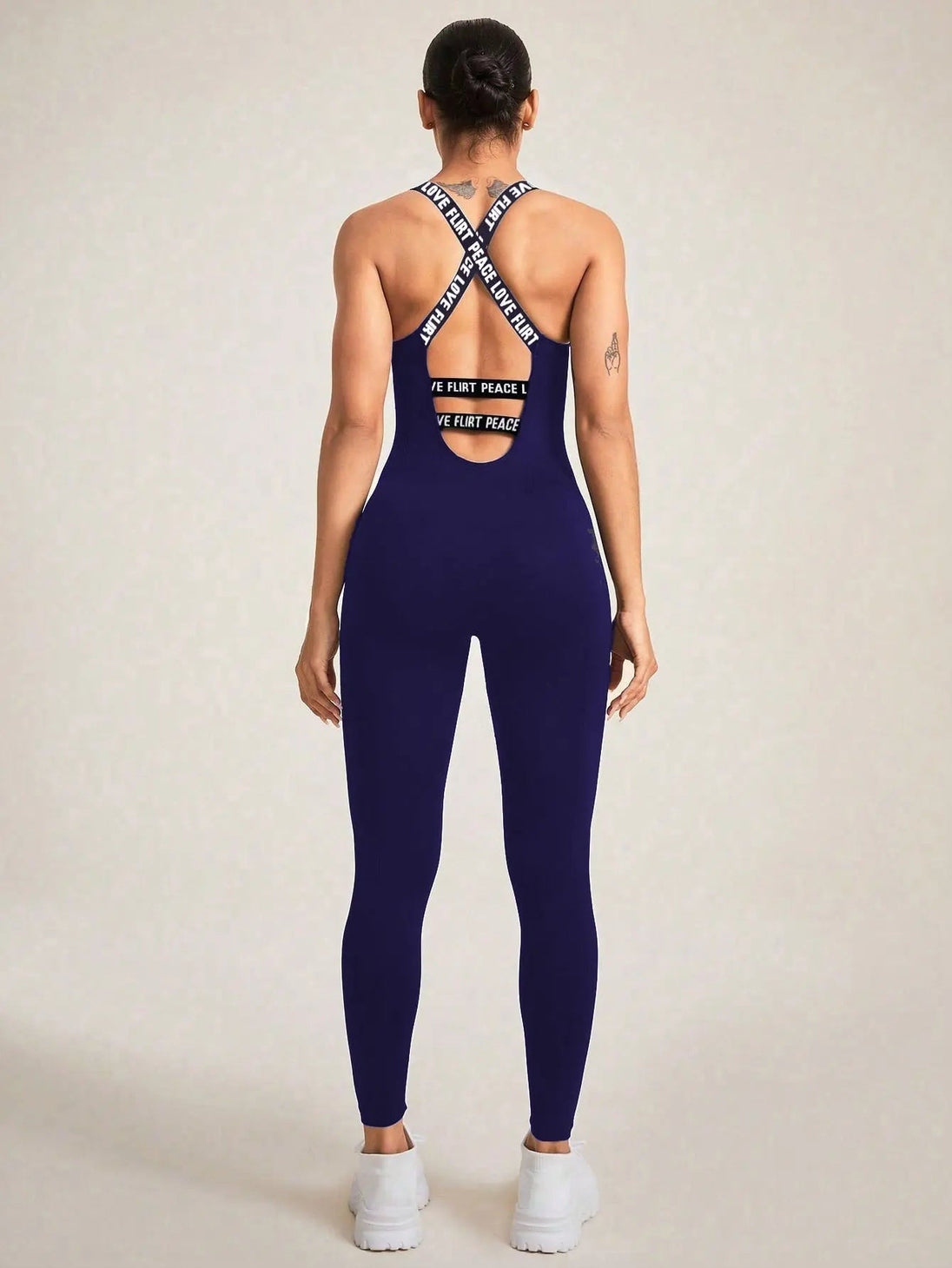 woman wearing seamless camisole jumpsuit in dark blue with crisscross back straps and white sneakers
