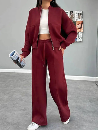Woman wearing a burgundy baseball collar zip up outerwear and drawstring pants set with white crop top and sneakers indoors