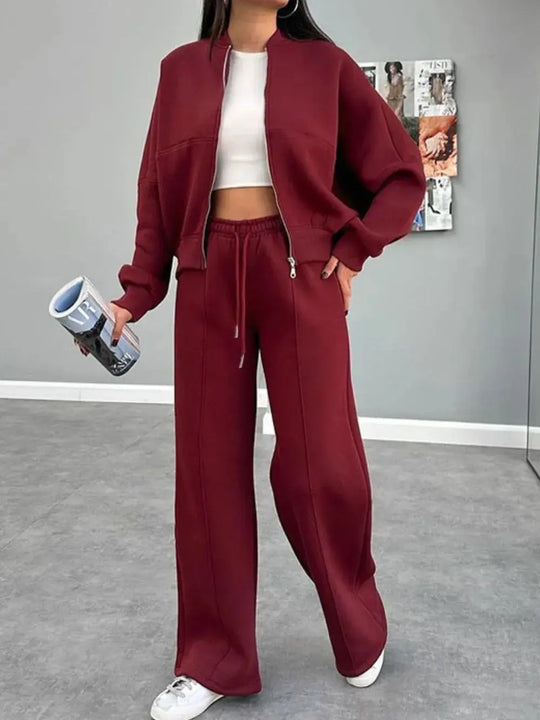 Woman wearing a burgundy baseball collar zip up outerwear and drawstring pants set with white crop top and sneakers indoors