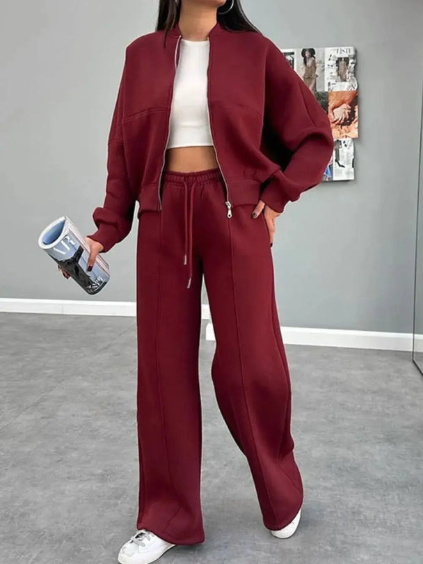 Woman wearing a burgundy baseball collar zip up outerwear and drawstring pants set with white crop top and sneakers indoors