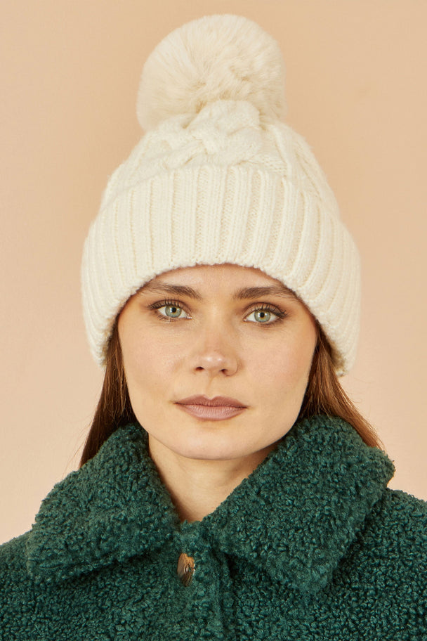 Yumi White Cable Knit Bobble Hat on woman wearing green coat