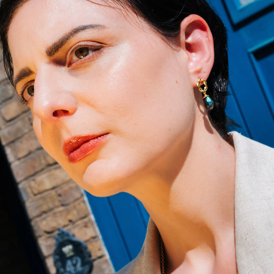 Close-up of woman wearing artisan handcrafted Moirai Twisted Loop Earrings with labradorite and 22K gold on recycled brass