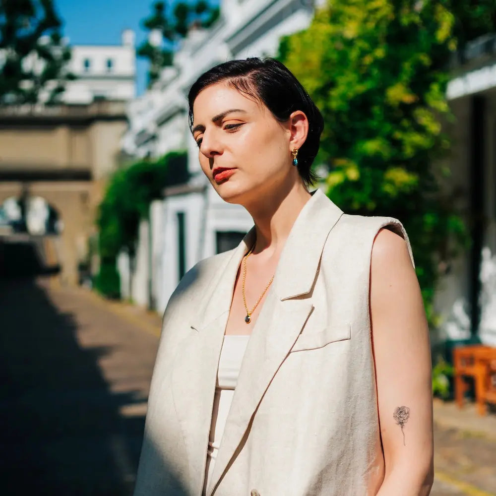 Woman wearing Moirai Twisted Loop Earrings with labradorite gemstones, 22k gold on recycled brass, outdoors in daylight