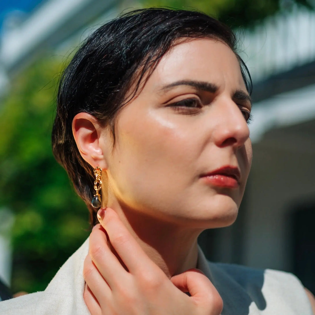 Woman wearing Moirai Double Twisted Loops Earrings with green onyx and 22k gold on recycled brass outdoors