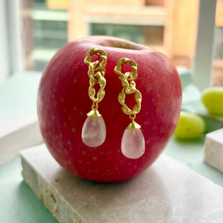 Moirai Double Twisted Loops Earrings with rose quartz drops and 22K gold on recycled brass displayed on red apple