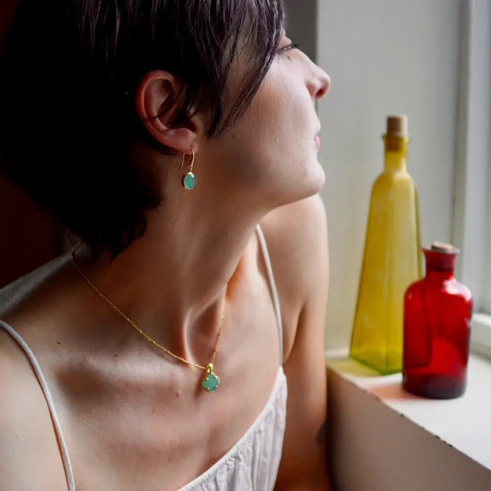 Charis Round Gemstone Earrings with Pariba Onyx in 22K gold on recycled brass worn by woman near window