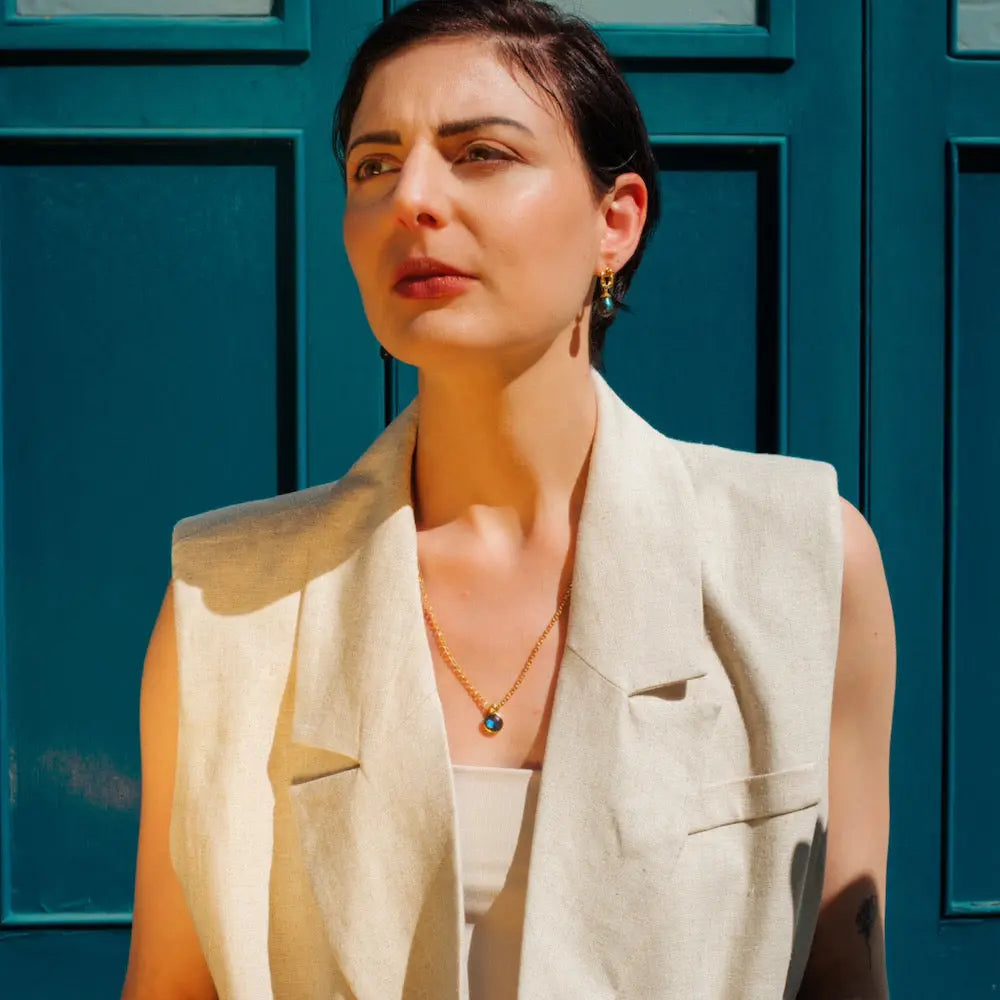 Woman wearing Moirai Twisted Loop Earrings with green onyx in gold setting against blue door background