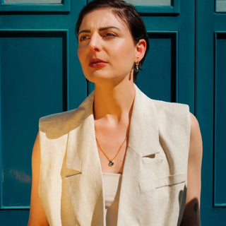 Woman wearing Moirai Twisted Loop Earrings with green onyx in gold setting against blue door background