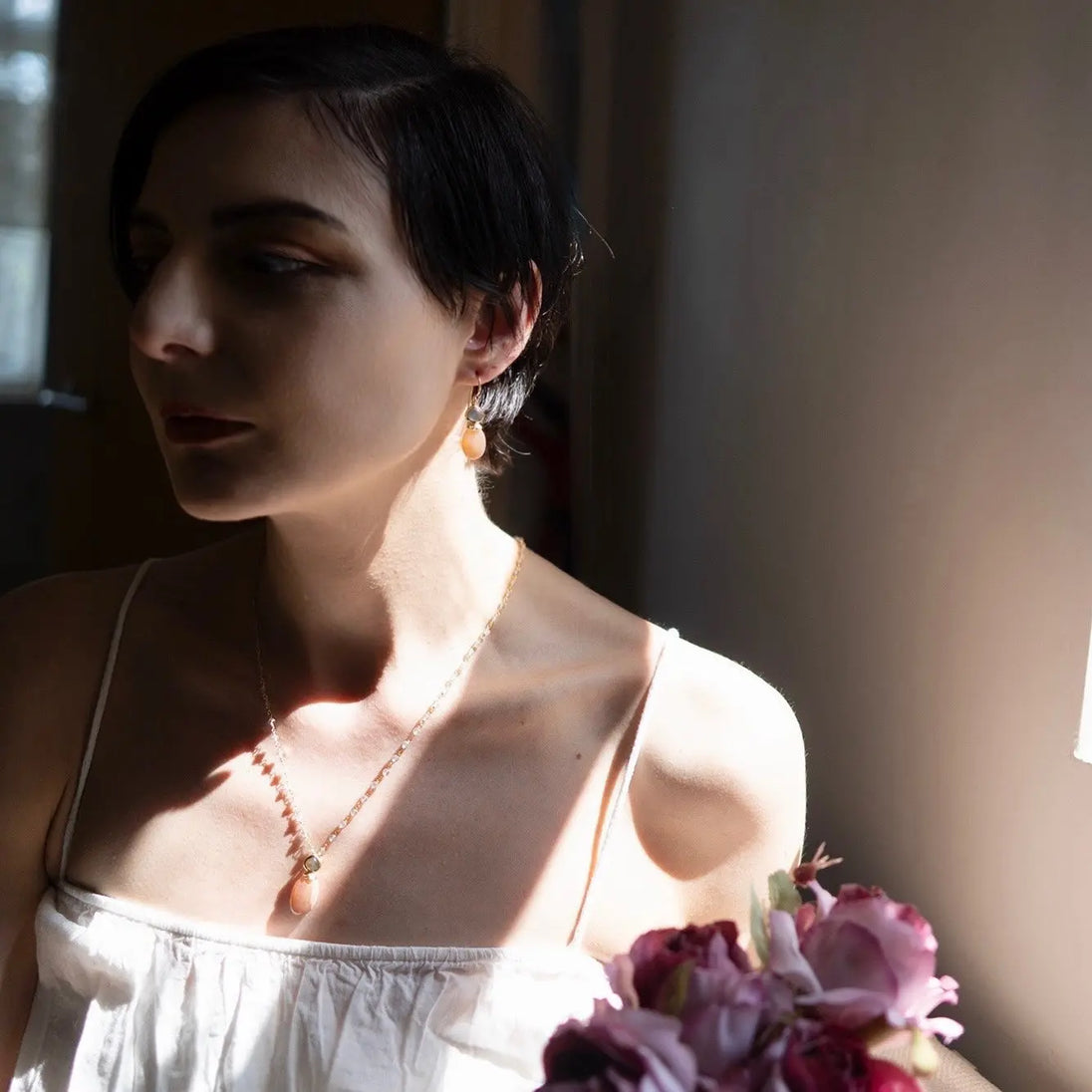 Woman wearing Persephone Double Gemstone Beaded Chain Necklace with peach moonstone and labradorite, 22K gold on recycled brass, in natural light near window