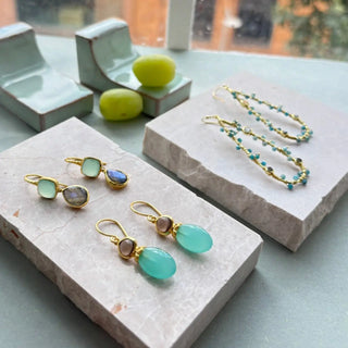 Persephone Double Gemstone Earrings with Pariba Onyx and Smoky Quartz in 22K gold on recycled brass, artisan handcrafted drop earrings displayed on stone trays.