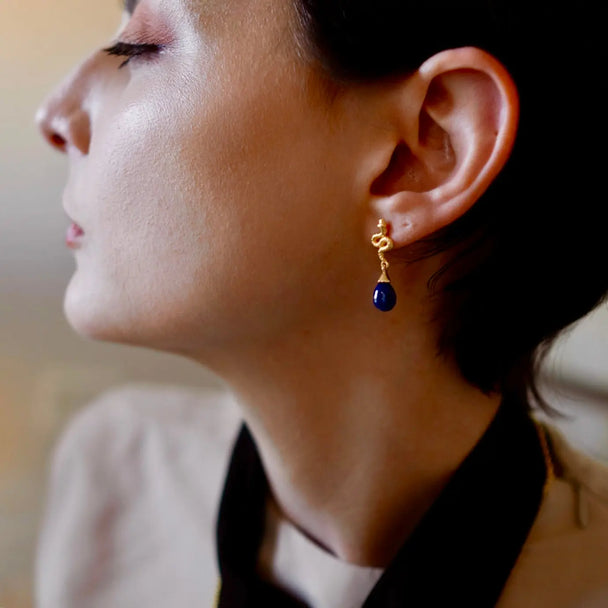 Close-up of a woman wearing Medusa Small Gemstone Drop Earrings with blue lapis stone and 22K gold detail