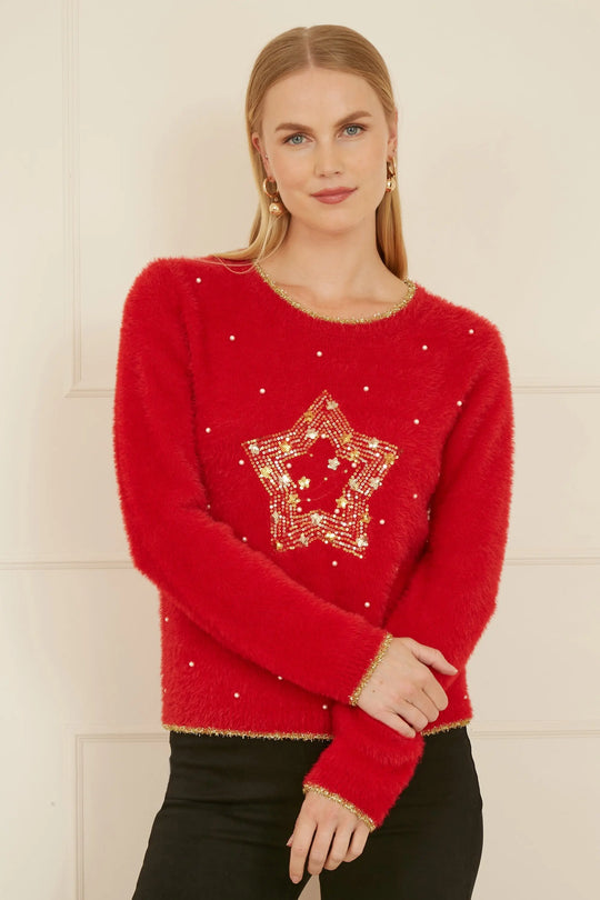 Woman wearing red knitted fluffy Christmas star jumper with gold embellishments and black pants