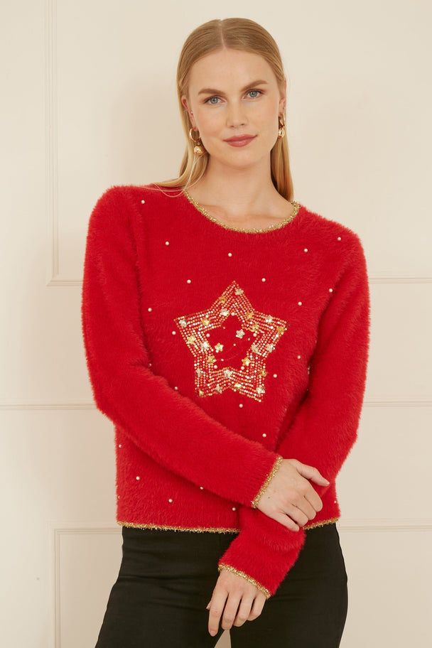 Woman wearing red knitted fluffy Christmas star jumper with gold embellishments and black pants