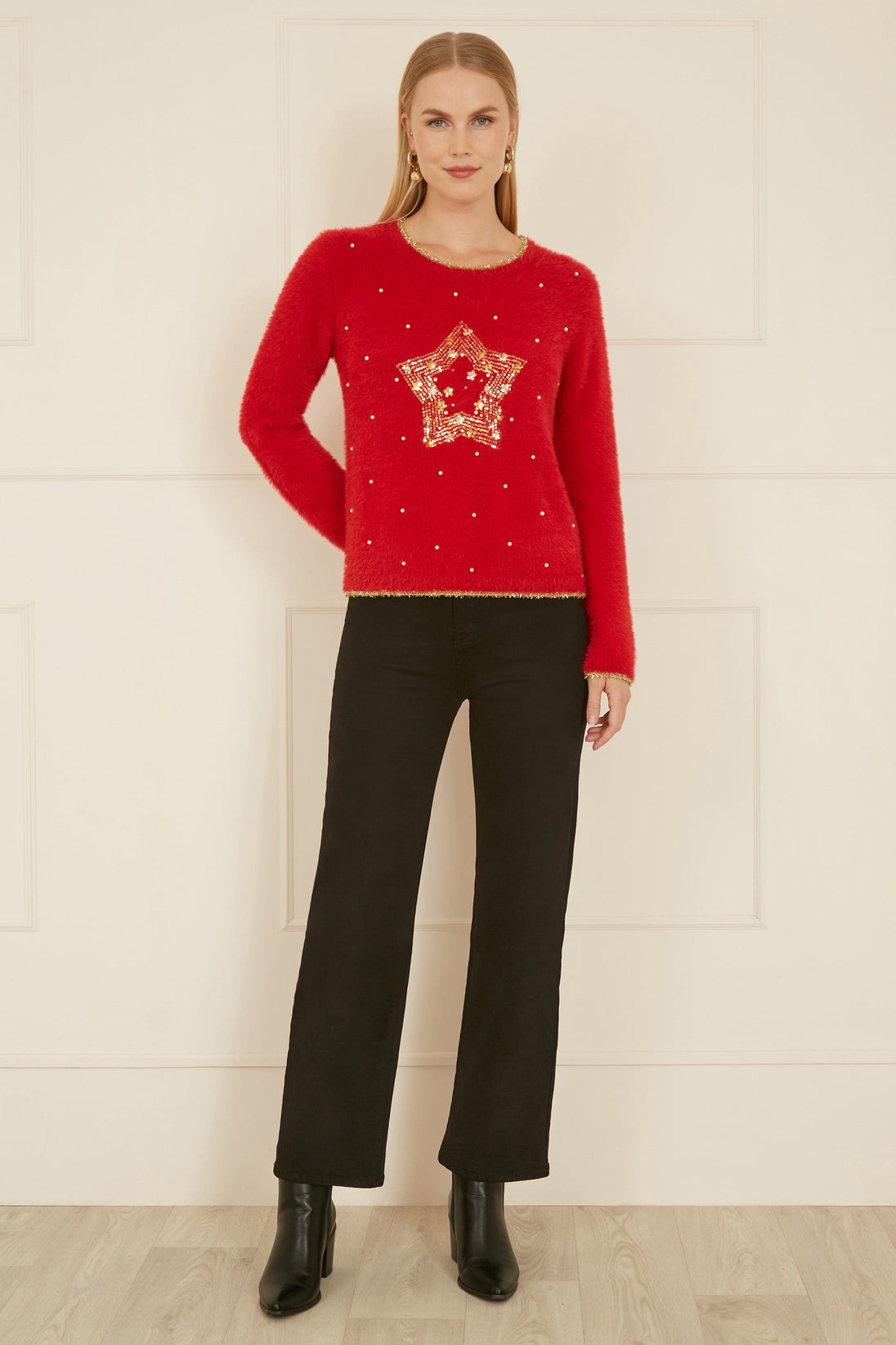 Woman wearing red knitted fluffy Christmas star jumper with gold embellishments paired with black pants and boots