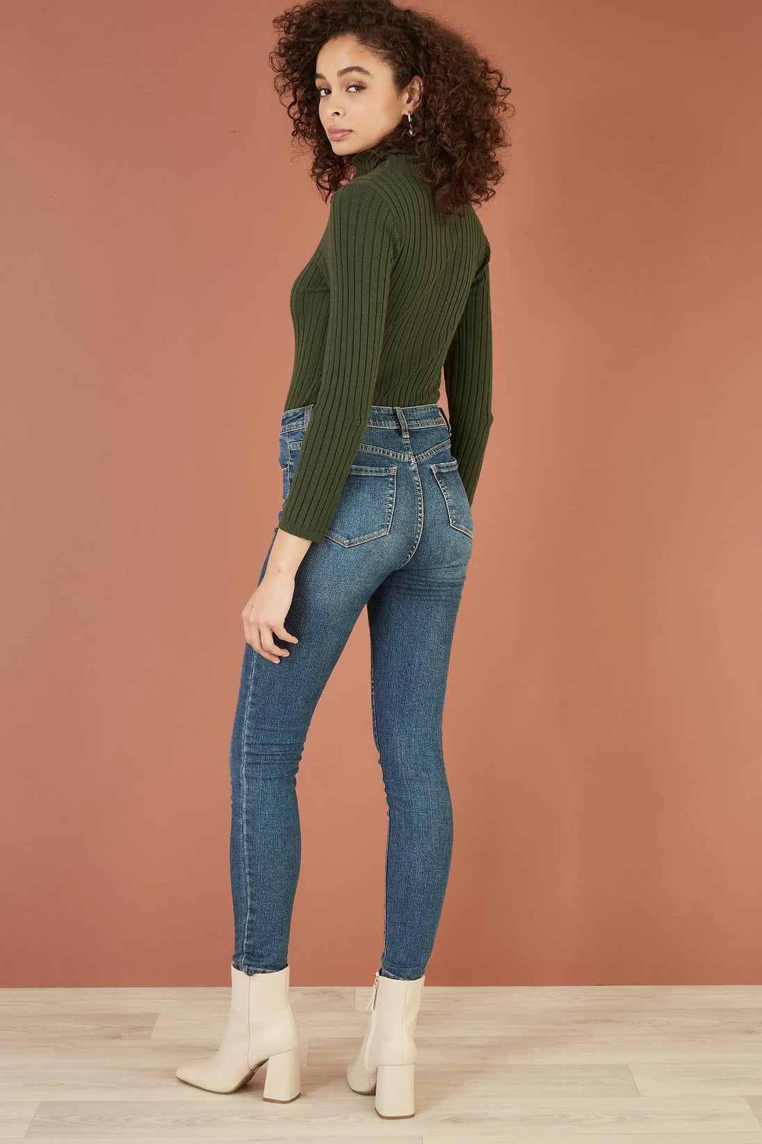 Woman wearing Yumi green ribbed knit roll neck jumper with fitted silhouette and blue skinny jeans.