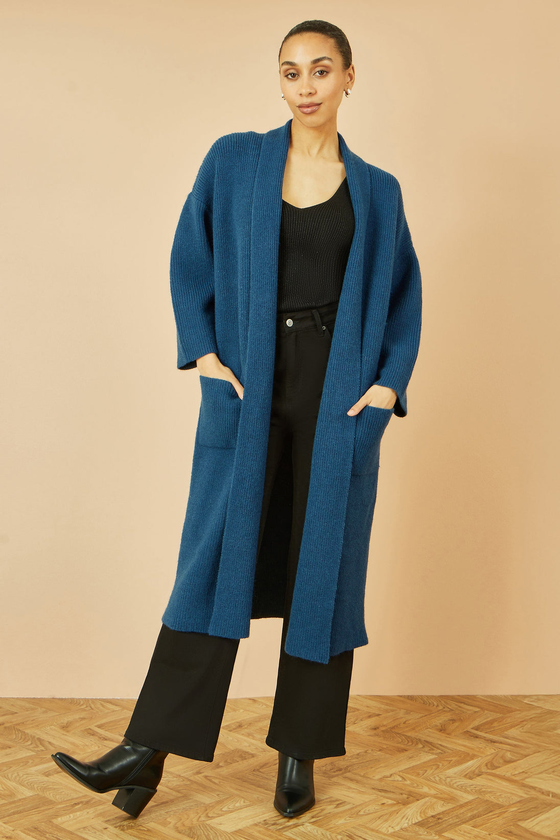 Yumi teal knitted maxi cardigan with pockets and ribbed detail worn with black outfit and ankle boots