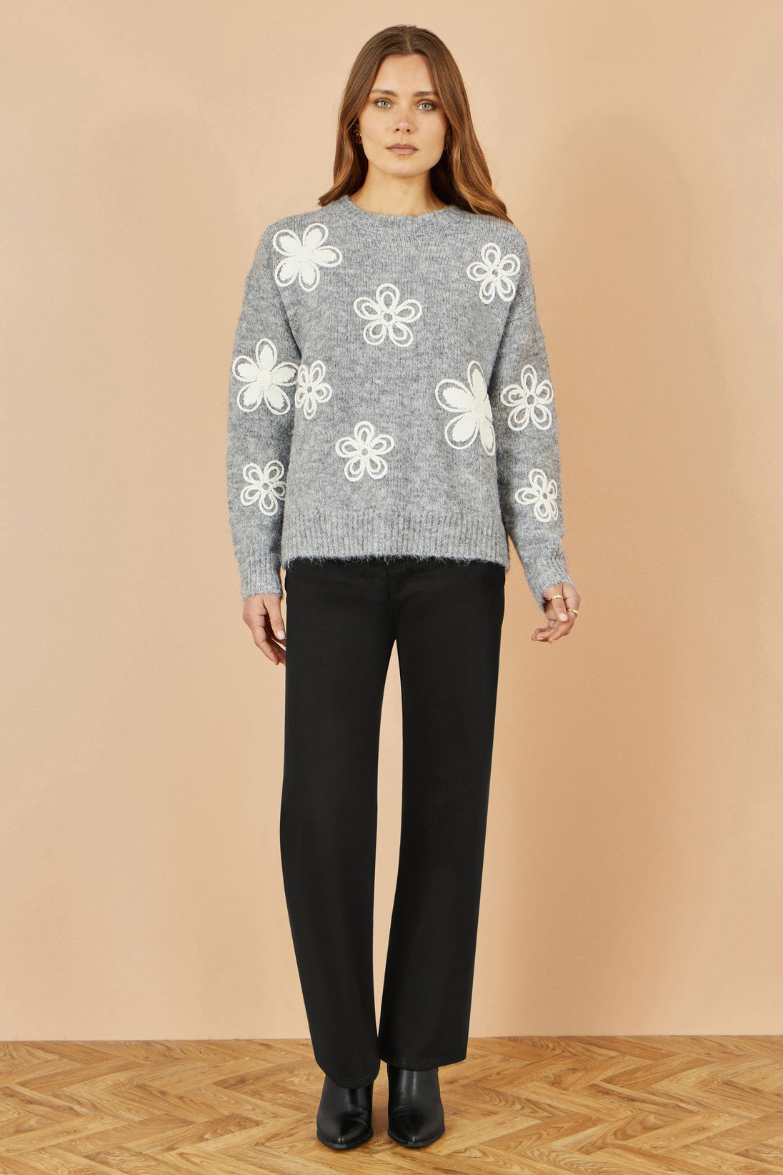 Yumi grey relaxed jumper with crochet flower details on model wearing black pants