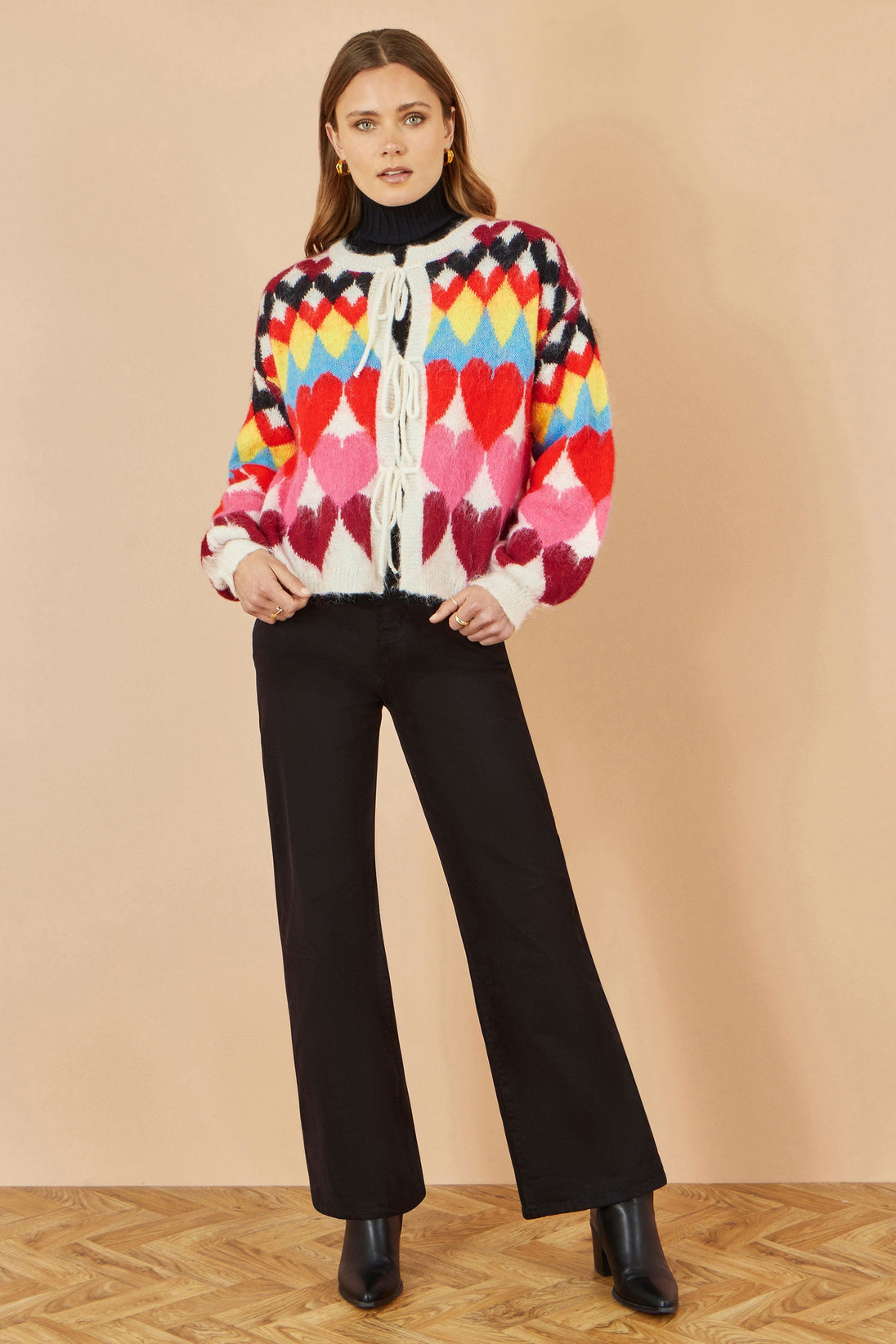Yumi Multicolour Tie Front Heart Intarsia Cardigan with bright heart pattern and tie front fastening worn with black pants