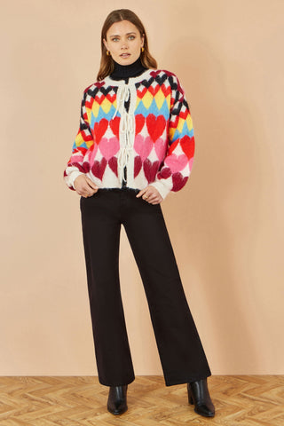 Yumi Multicolour Tie Front Heart Intarsia Cardigan with bright heart pattern and tie front fastening worn with black pants