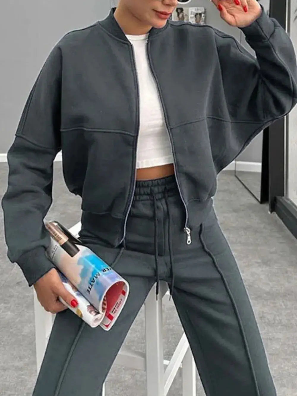 Woman wearing dark gray baseball collar zip up outerwear and matching drawstring pants set with white crop top