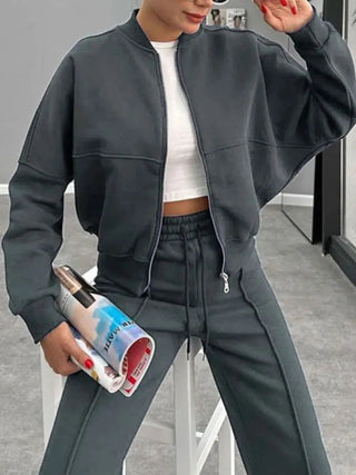 Woman wearing dark gray baseball collar zip up outerwear and matching drawstring pants set with white crop top