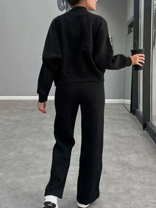 Woman wearing black baseball collar zip up outerwear and drawstring pants set with a cup in hand.
