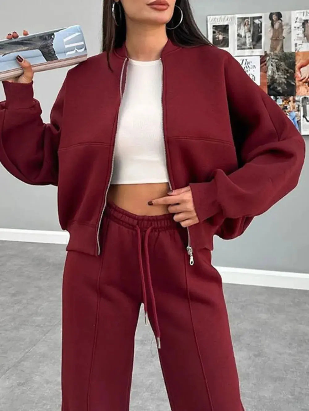 Woman wearing maroon baseball collar zip up outerwear and drawstring pants set with white crop top indoors