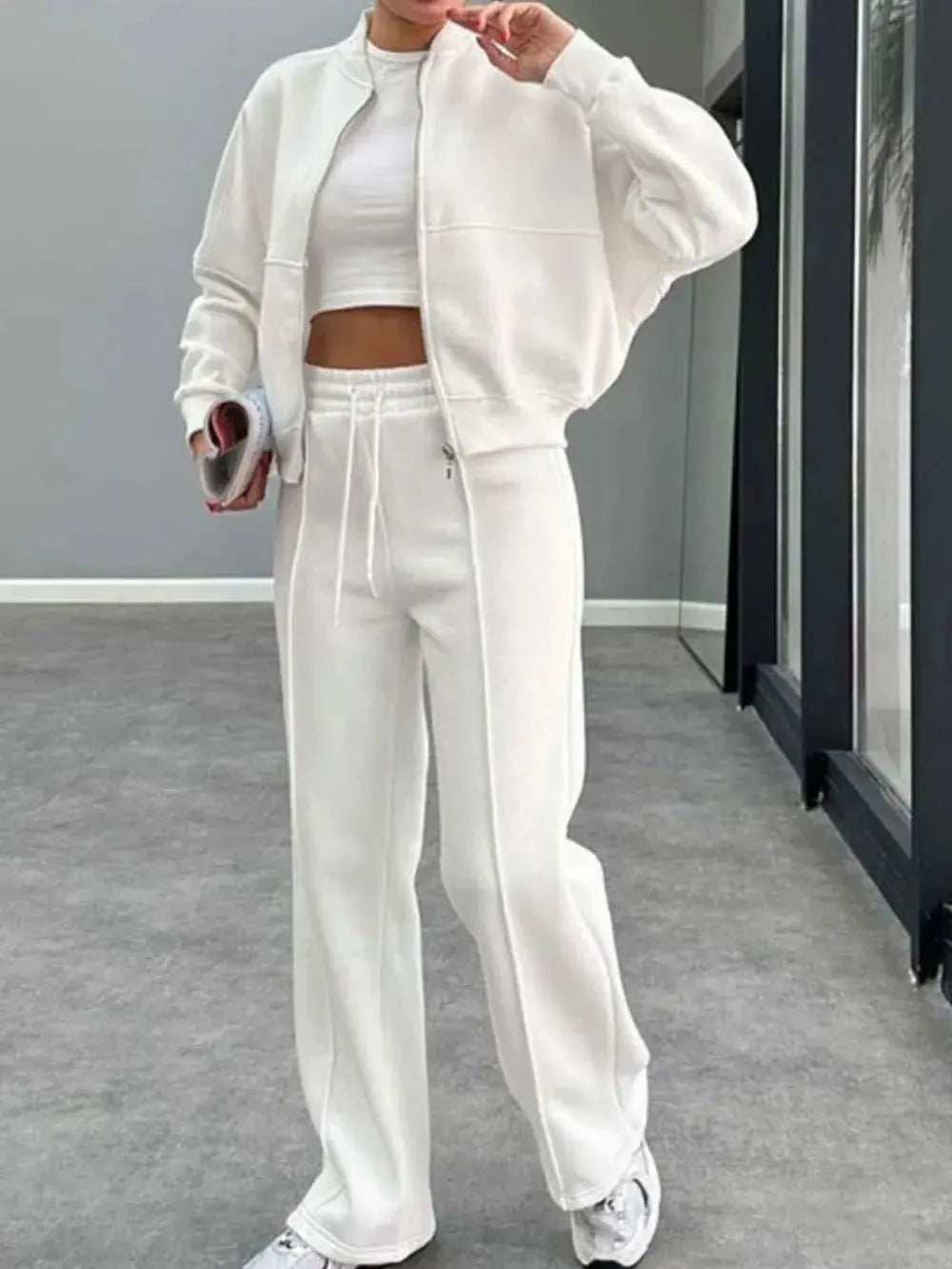 Woman wearing white baseball collar zip up outerwear and drawstring pants set with crop top and sneakers indoors