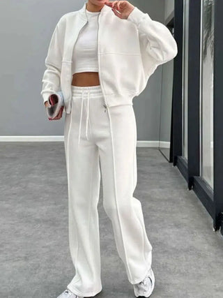 Woman wearing white baseball collar zip up outerwear and drawstring pants set with crop top and sneakers indoors