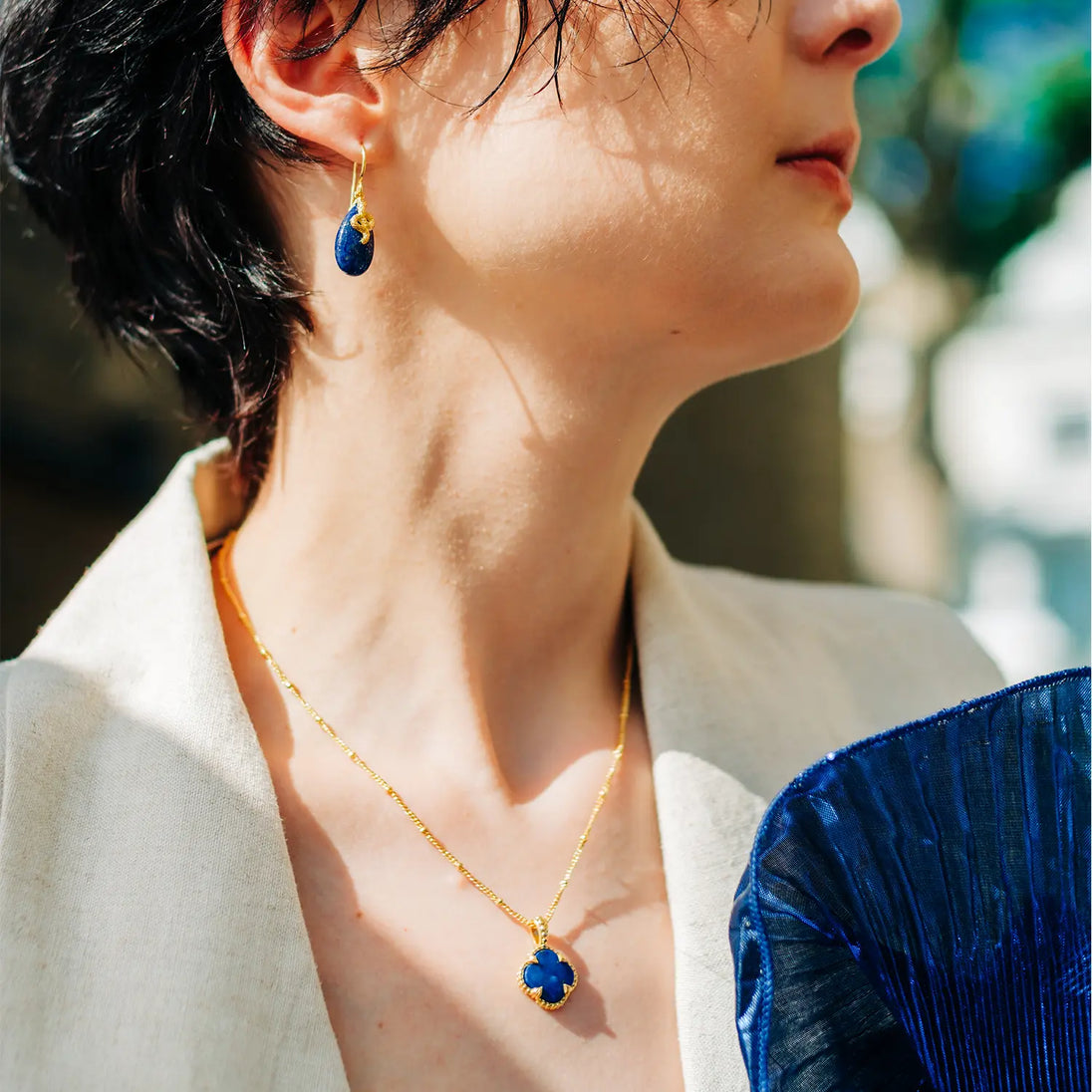 Tyche Gemstone Necklace with Pariba Onyx pendant in 22K gold on recycled brass, worn by woman outdoors