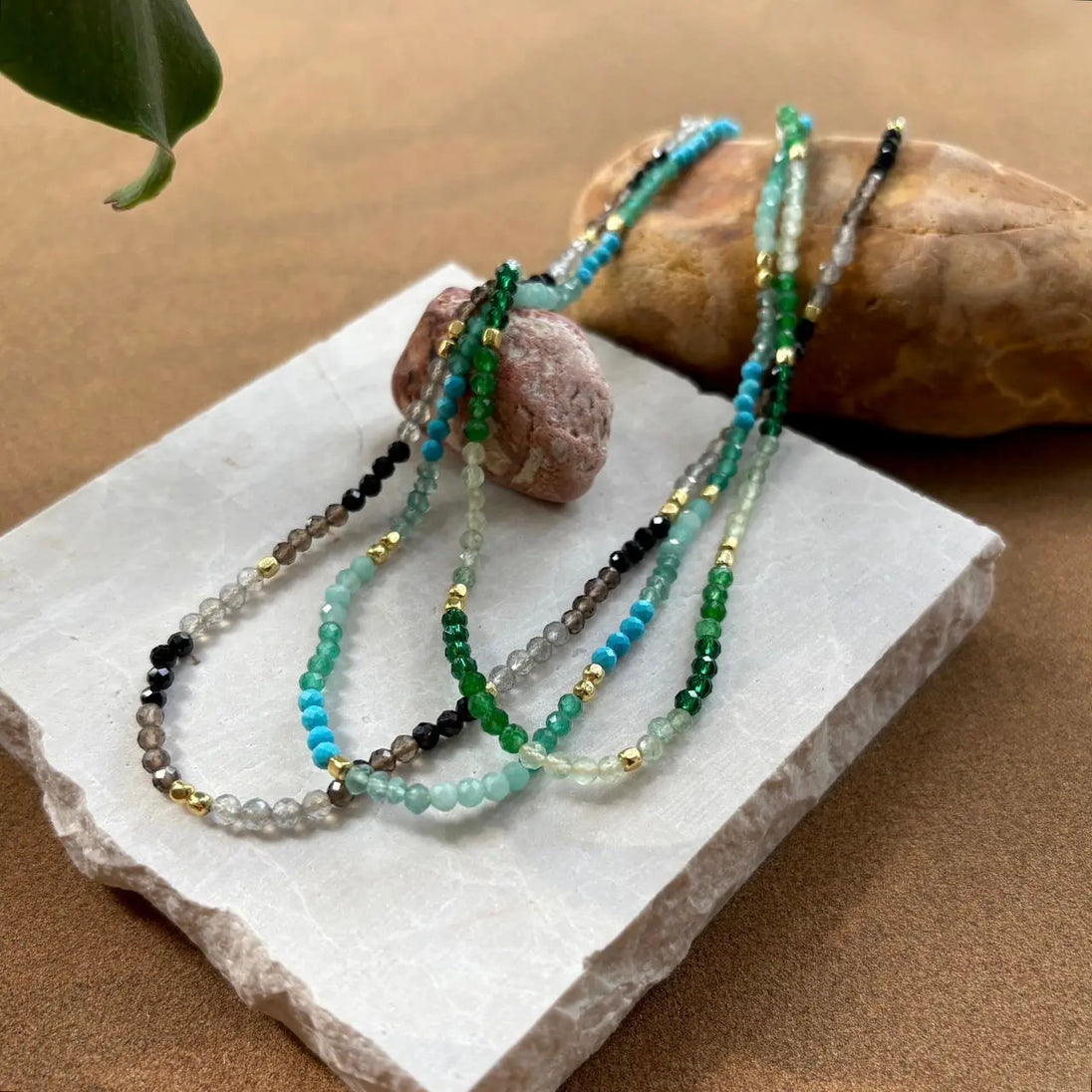 Milos Mixed Gemstone Beaded Necklace with Prehnite, Moss Agate, Green Aventurine, and 22K gold accents displayed on stone slab