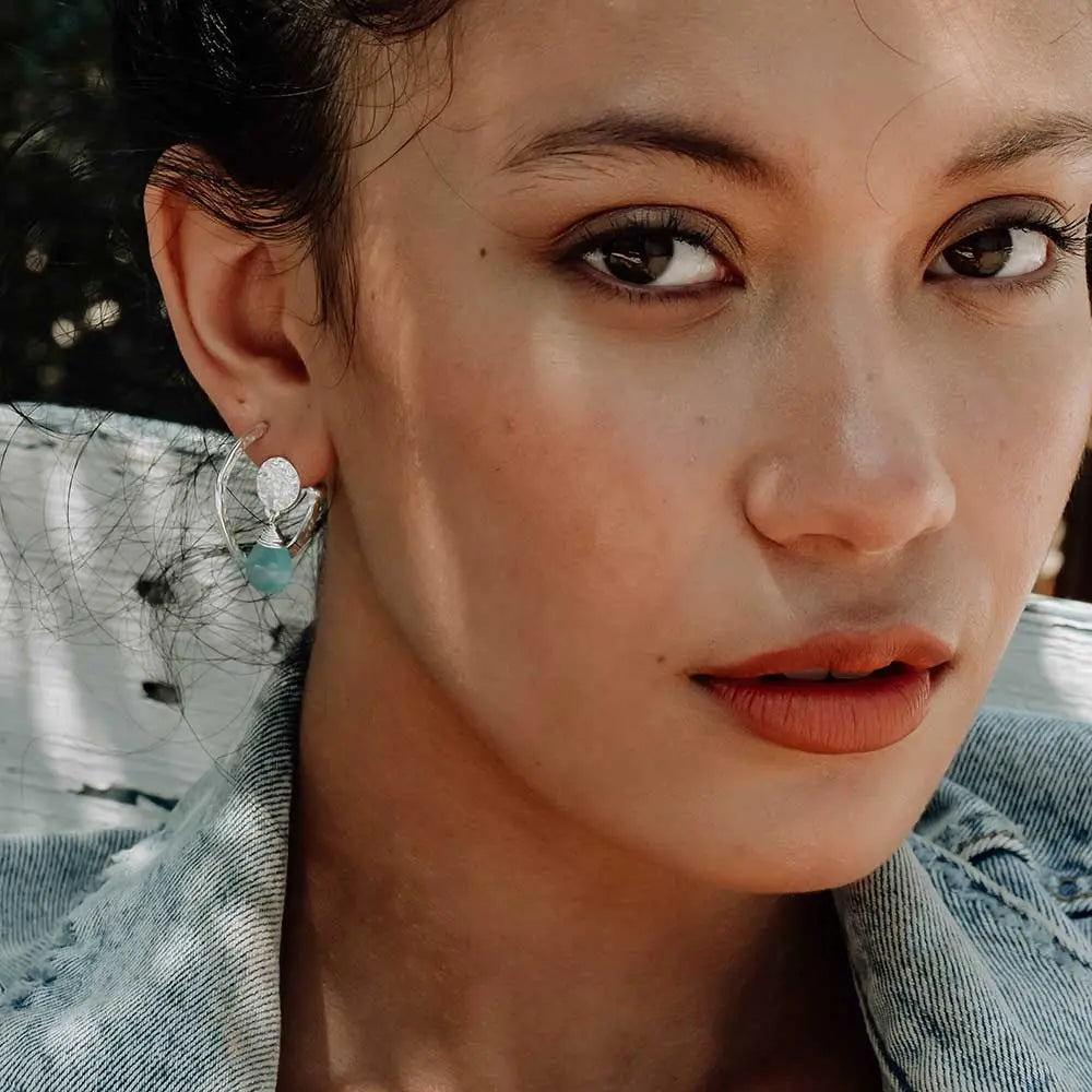 Close-up of a woman wearing Classic Athena Drop Earrings with silver coin studs and aqua Pariba onyx gemstones.