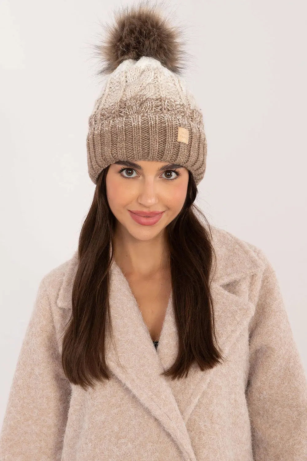 Beige two tone winter beanie with pom-pom and fleece lining on model wearing beige coat