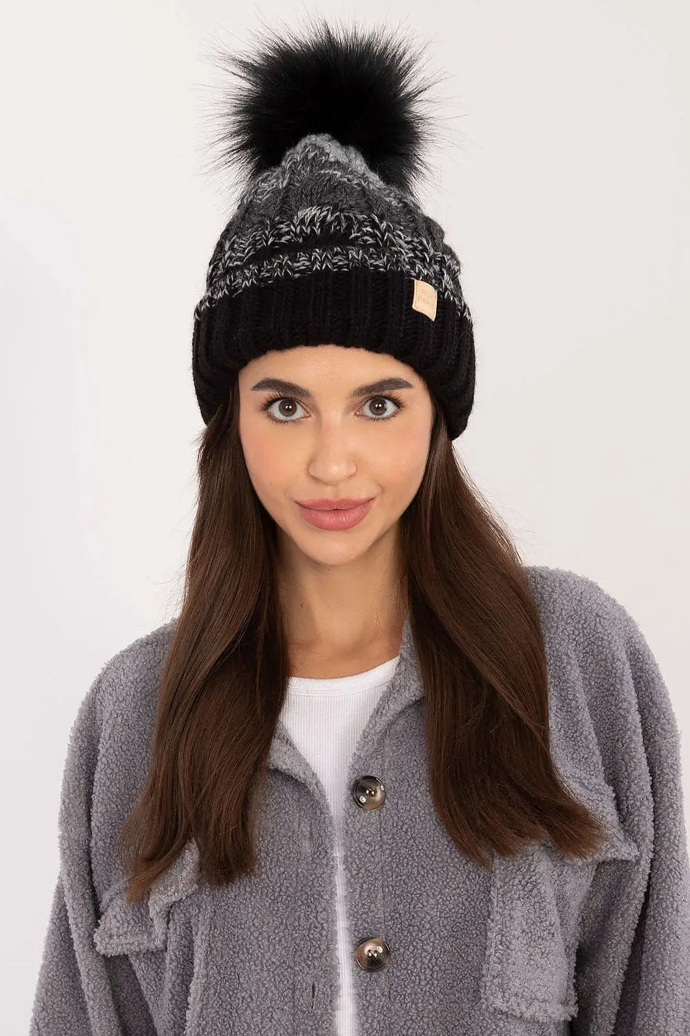 Woman wearing a black and gray two-tone winter beanie with pom-pom and plaid pattern