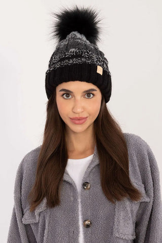 Woman wearing a black and gray two-tone winter beanie with pom-pom and plaid pattern