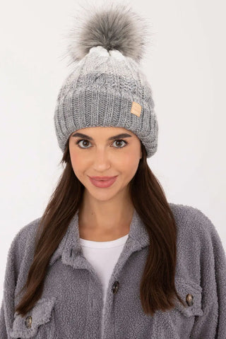 beige two tone winter beanie with plaid pattern and pom-pom on woman wearing fleece jacket