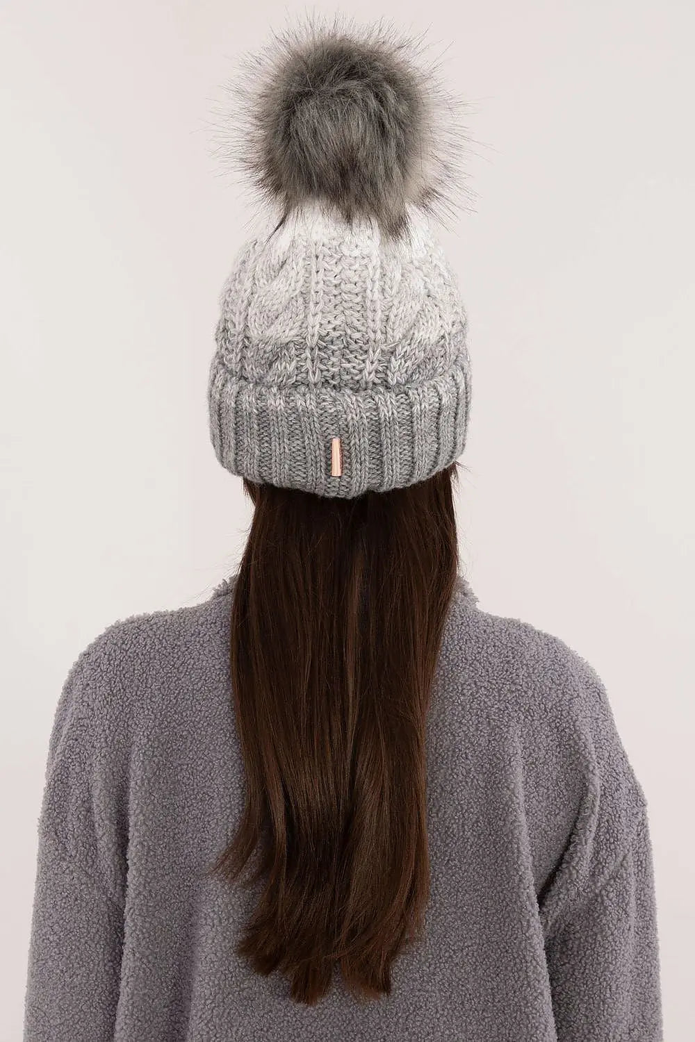 Beige two tone winter beanie with fluffy pom-pom and fleece lining on woman with long hair