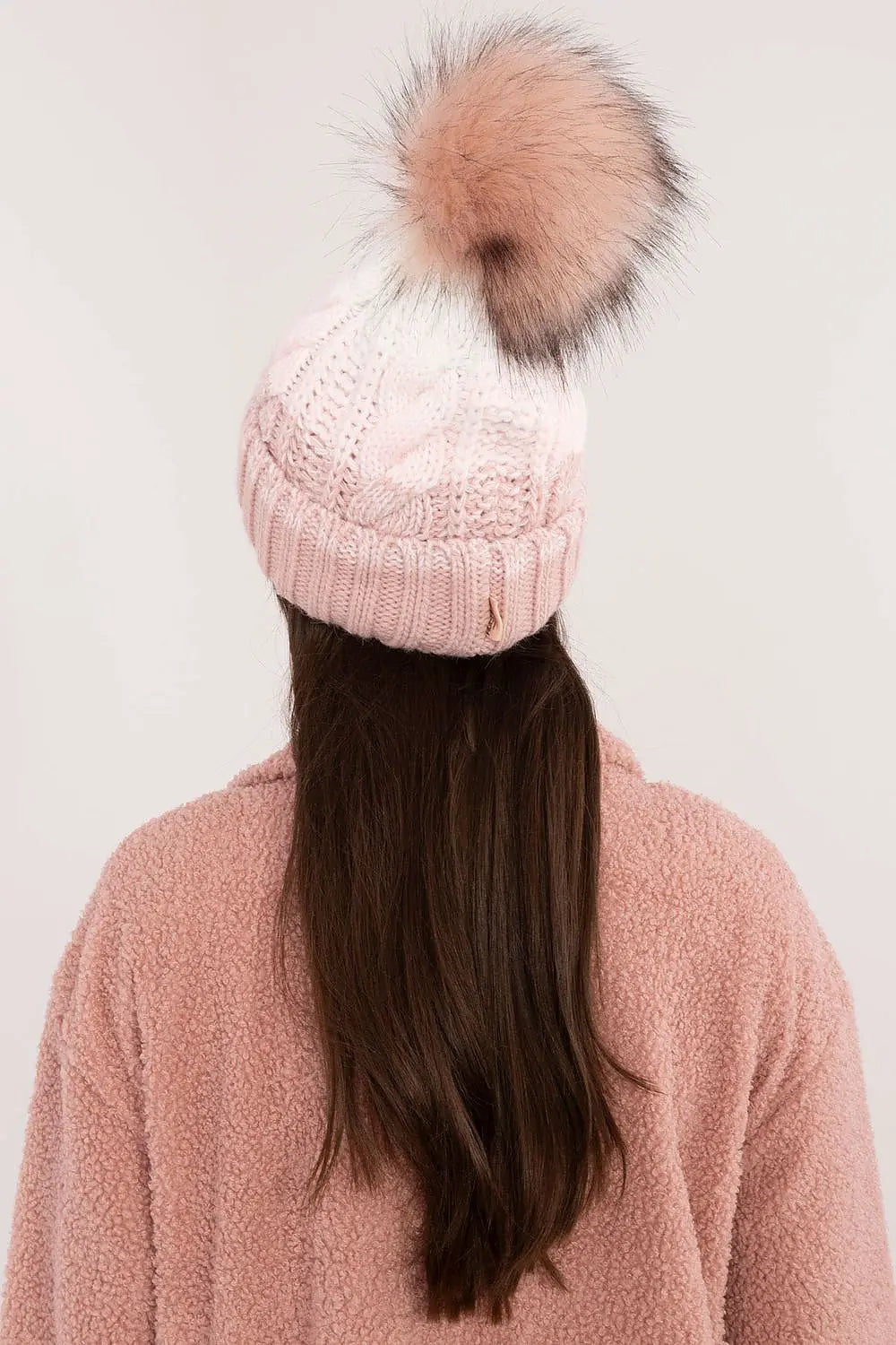 Beige two tone winter beanie with pom-pom and fleece lining on woman wearing pink jacket