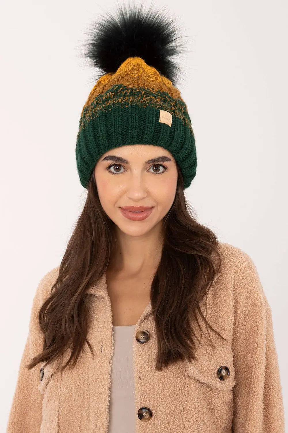 Beige two tone winter beanie with plaid pattern and fluffy pom-pom on woman wearing cozy jacket