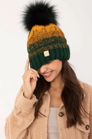 Woman wearing green and mustard winter beanie with black pom-pom and beige coat