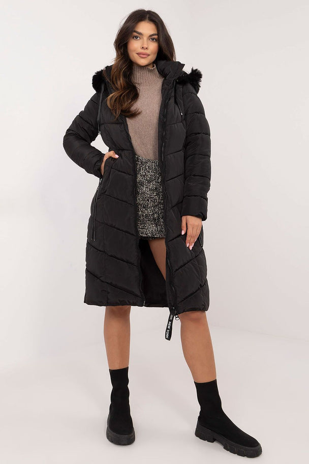 Woman wearing a black long quilted down jacket with detachable fur hood and zipper closure